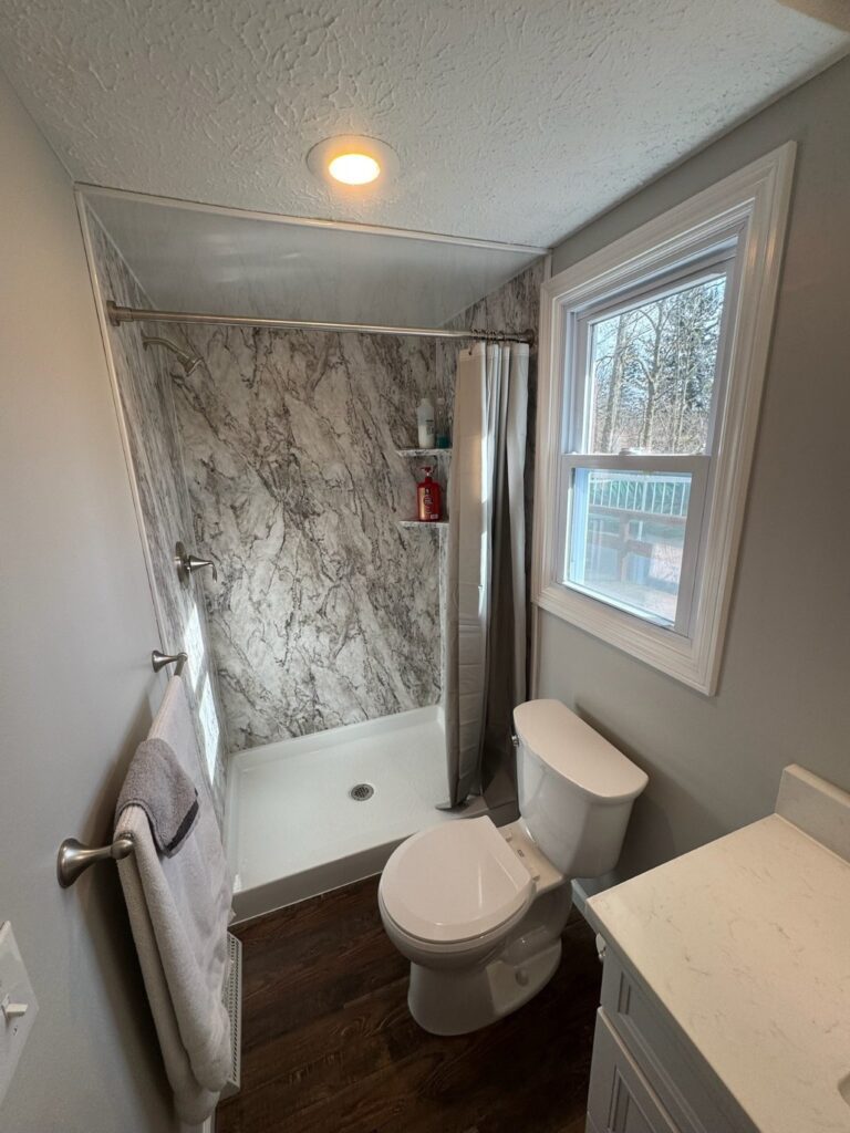A small bathroom with a shower, toilet, and sink under natural light.