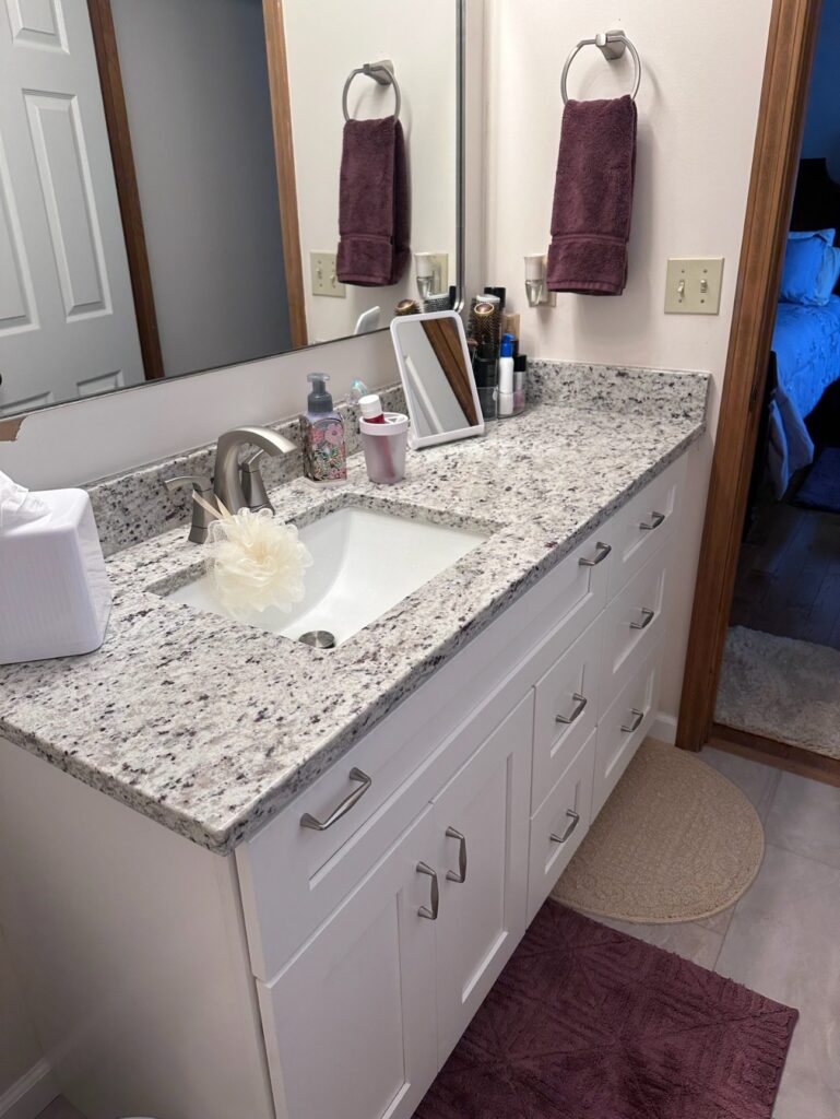 Clean bathroom sink area with granite countertop and white cabinets.